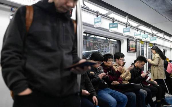Gambar fail menunjukkan sejumlah penumpang menggunakan telefon bimbit keluaran China di dalam tren di Beijing baru-baru ini. - Foto AFP