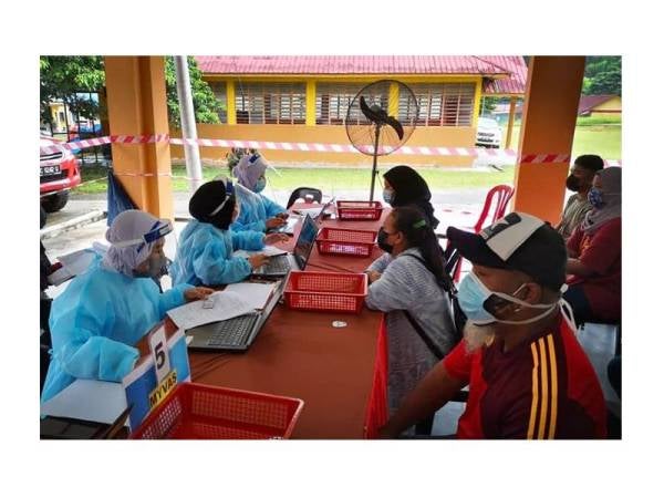 Petugas KKM membantu masyarakat orang asli di sekitar Gua Musang di kaunter pendaftaran sebelum menerima suntikan vaksin. 
