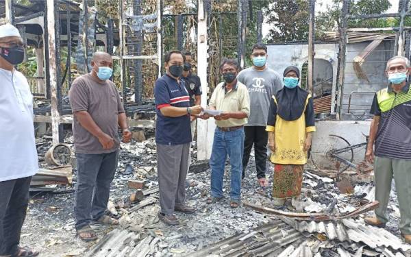Ahmad (tiga dari kiri) menyerahkan sumbangan kepada mangsa kebakaran Abdullah di Jalan Parit Baran Sangkar Dua Ayer Baloi pada Jumaat.