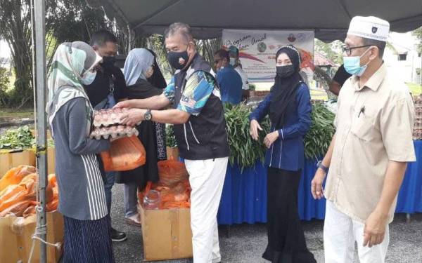 Che Zakaria (kiri) memberikan ayam, telur, gula dan sayur kepada orang ramai yang membeli empat barangan itu dengan harga RM10 pada Program Jualan Amal di Permas Jaya, Pasir Gudang pada Selasa.