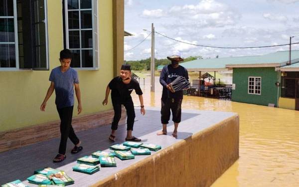 Pelajar cuba mengeringkan bahan bacaan, buku dan kitab yang basah akibat banjir.