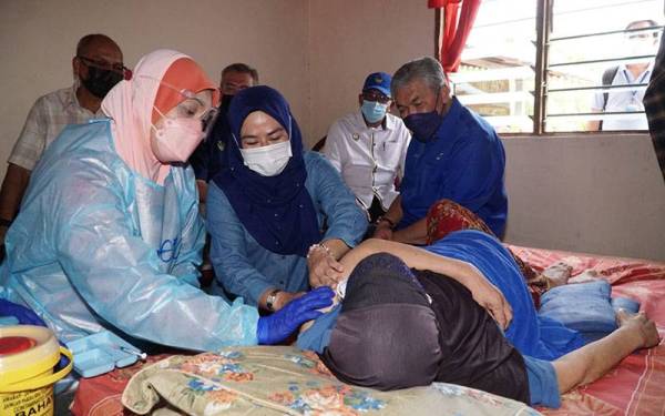 Noraini (tengah) bersama Ahmad Zahid (kanan) melihat vaksinasi dilakukan kepada Salamah Anang, 64, pada program 'outreach' HCTM UKM di Parlimen Bagan Datuk pada Sabtu.