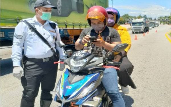 Seorang penunggang motosikal, Muhmamad Nur Mustaqim Abdul Wahab dari Johor menunjukkan aplikasi MySejahtera kepada seorang anggota polis di Plaza Tol Ayer Keroh, pada Isnin. 