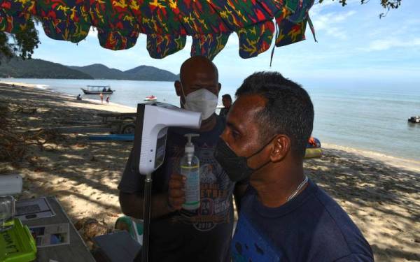 Seorang pengunjung pantai Batu Ferriinghi mengambil suhu badan sambil dipantau oleh budak pantai atau beach boy Azmil Zulkifli Balakrishnan, 36, sebagai salah satu langkah prosedur operasi standard (SOP) hari ini.