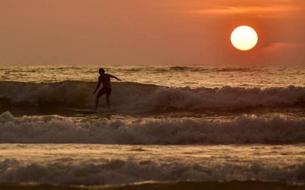 Seorang lelaki bermain papan luncur air di tengah gelombang ombak besar ketika tinjauan di Pantai Sungai Pagar hari ini.