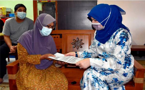 Rina (kanan) menyampaikan surat kelulusan bantuan kanak-kanak berjumlah RM300 sebulan kepada penerima bantuan Narriman Husin, 56, (tengah) ketika melakukan lawatan ke rumah beliau di Jalan Cheng Lama, pada Selasa. - Foto Bernama