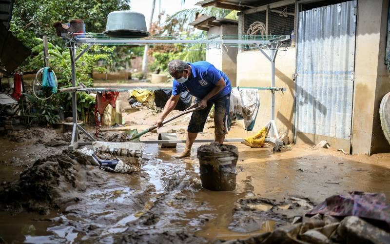 Amzaini Nayan, 59, membersihkan kawasan halaman rumahnya yang diselaputi lumpur akibat dilanda banjir kilat petang semalam di Kampung Seberang Pekan, Yan pada Khamis. - Foto Bernama
