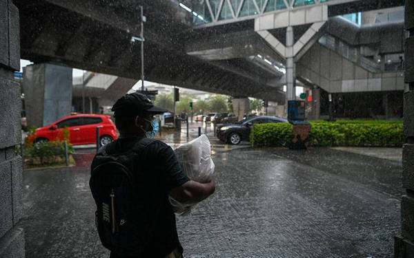 Seorang lelaki berteduh daripada cuaca hujan ketika tinjauan di sekitar ibu kota hari ini.