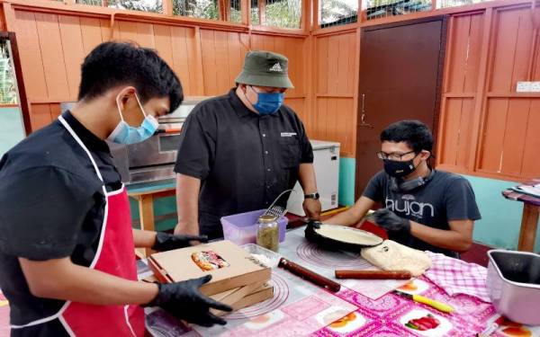 Noor Akmal (tengah) melihat pekerjanya menyiapkan tempahan pizza