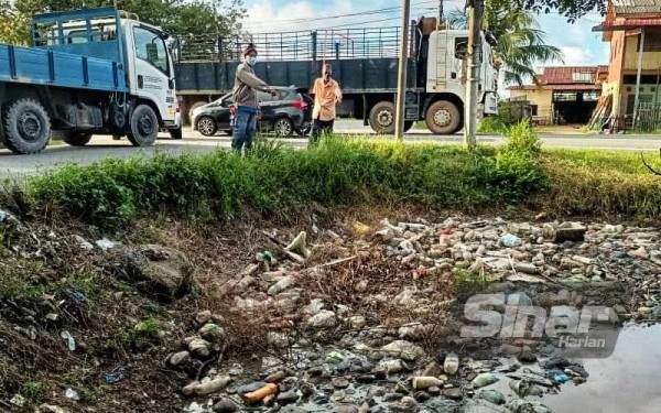Halim (kiri) menunjukkan antara saliran yang dipenuhi sampah sarap di Batu 8 Jalan Tokai di sini pada Selasa.