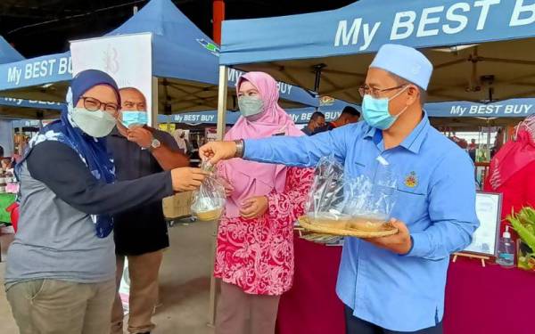 Tuan Saripudin (kanan) mengagihkan bubur jagung percuma kepada orang ramai sempena pelancaran My Best Buy di Pusat Transformasi Luar Bandar (RTC) Tunjong pada Jumaat.