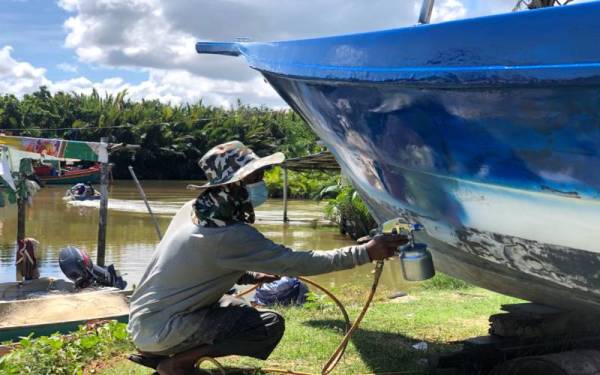 Mustaqim melakukan kerja-kerja mengecat dan membaiki bot pelanggan pada musim tengkujuh.