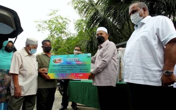 Idris (dua, kanan) menyampaikan replika pakej bantuan kelestarian perniagaan berjumlah RM5,000 kepada peniaga pisang goreng Azidi Sudin (tiga, kiri) pada Program Inspirasiku MyHAUS anjuran YaPEIM di Kampung Seri Aman Menglembu hari ini. Foto Bernama