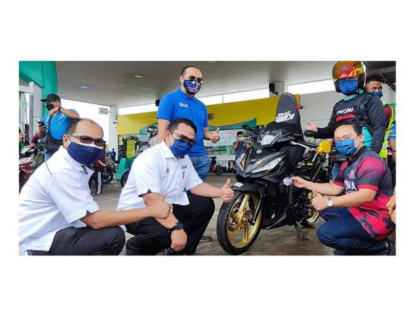 Wan Saiful (kanan) menampal pelekat kempen menyimpan bersama PTPTN pada sebuah motosikal penerima Program Minyak Motor Percuma di Jitra pada Sabtu. Turut kelihatan (duduk dari kiri) Syerman dan Esrifaridz.