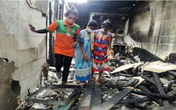 Vijaya (tengah) bersama dua anaknya ketika meninjau sekitar rumahnya selepas kejadian.