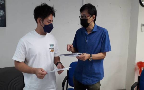 Chee Boon (kanan) dan Kai Cheng menunjukkan poster dan salinan laporan polis di Pejabat Biro MCA Penyelarasan Hal Ehwal Kerajaan di Taman Maju, Johor Bahru pada Sabtu.