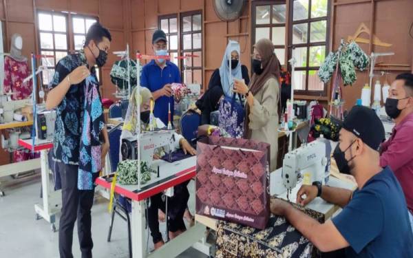 Azrool Izdwan (kiri) mendengar penerangan daripada Rosnah (tiga dari kanan) berhubung produk batik yang dihasilkan di Bengkel Liyana Batique Collections, Pusat Komuniti Kreatif Kampung Lebai Saman, Naka, Kuala Nerang baru-baru ini.