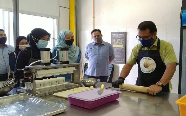 Zainol Fadzi (kanan) mencuba sendiri cara pembuatan karipap keluaran sebuah syarikat ketika mengadakanlawatan sempena Program Lonjakan Usahawan IKS Halal Park Tambun di Halal Park Tambun, di sini pada Isnin.
