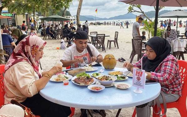 Muhammad Shaharudin (tengah) bersama isteri dan anaknya menikmati hidangan siakap bakar sambal di Pantai Chenang, Langkawi pada Rabu.