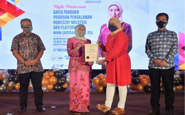 Nancy (dua, kiri) menyampaikan sijil pendaftaran peserta program pengalaman homestay Malaysia kepada Pengusaha Homestay Sadong Jaya, Suraya Lariwoo (dua, kanan) pada Majlis Pelancaran Garis Panduan Program Pengalaman Homestay Malaysia dan Platform jomhomestay.my, pada Sabtu.- Foto Bernama