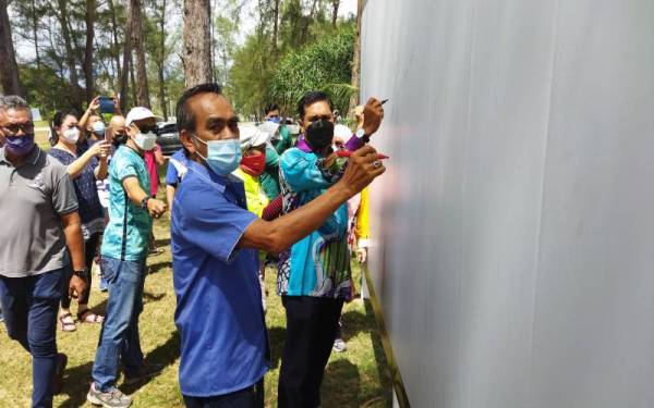 Hamdan (kanan) menandatangani gegantung yang disediakan sebagai tanda sokongan kepada Kempen Sayangi Pokok ' Selamatkan Pokok Kita' yang diadakan di Pantai Sepat, Kuantan pada Ahad.