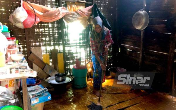 Mazita mengemop lantai dapur yang dibasahi hujan akibat atap rumah yang bocor. - FOTO SINAR HARIAN
