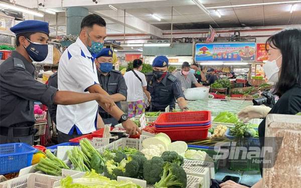 Mohd Ridzuan (dua dari kiri) sedang bertanya mengenai harga sayur-sayuran kepada peniaga di Pasar Bayan Baru pada Rabu.