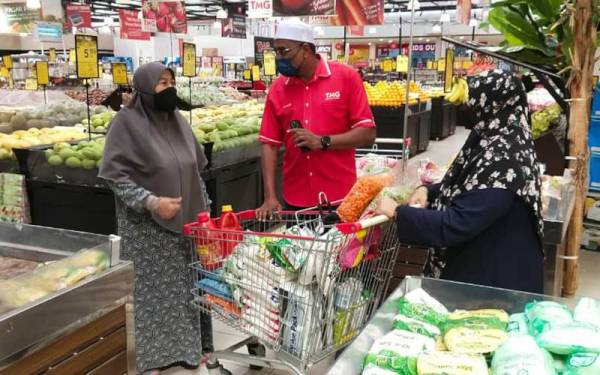 Hasnah (kiri) mendengar penjelasan Muhammad Hidir Ravi berhubung Program Jualan #Keluarga Malaysia di TMG Mall Tanjung Lumpur, Kuantan pada Sabtu.