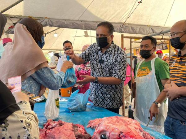 Reezal Merican menyerahkan bungkusan daging lembu kepada pembeli di Jualan Murah Keluarga Malaysia di Kepala Batas pada Ahad.