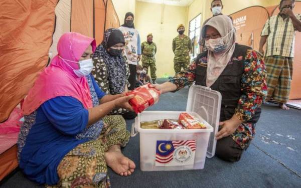 Sukarelawan JKM, Lina Mohd Zainudin (kanan) menyampaikan bakul makanan kepada mangsa banjir Mek Yeam Ahmad, 80, di PPS Sekolah Kebangsaan (SK) Tok Deh dekat Rantau Panjang. - Foto Bernama