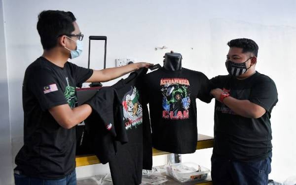 Mohd Hafiz Almuhaimi (kanan) berbincang mengenai rekaan baju terkini bersama pembekal Wan Hazmin Wan Osman sebelum menjualnya menerusi aplikasi dalam talian semasa ditemui. - Foto Bernama
