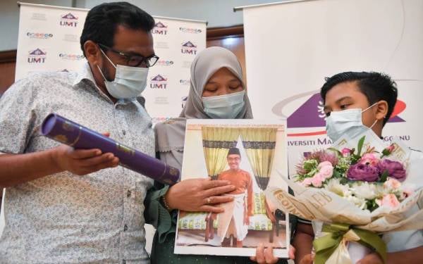 Ibu bapa kepada graduan UMT, Allahyarham Muhammad Amirul Bakhtiar, Rozaina Wahab, 48, dan Adnan Endut, 57, bersama skrol Ijazah Sarjana Muda Sains Agro Teknologi (Akuakultur) dan gambar anak mereka pada Majlis Konvokesyen UMT ke-18 (Siri Kedua) di UMT pada Ahad. - Foto Bernama