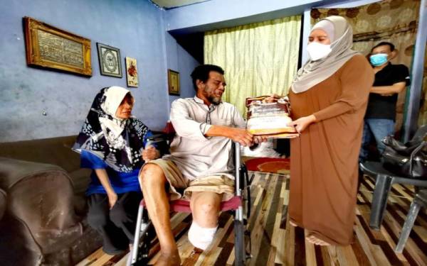 Pengerusi Perkasih, Norfadilah Mansor memberi bantuan beras kepada Mustafa sambil diperhatikan Zaiton.