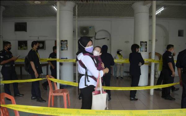 Anggota polis, lynne Ginju Law membawa anaknya Fatimah Sopiah Kama Farkhan ketika menunaikan tanggungjawab pada pengundian awal bagi PRN Sarawak ke-12 di Dewan Serbaguna Ibu Pejabat Polis Kontinjen Sarawak pada Selasa. - Foto Bernama