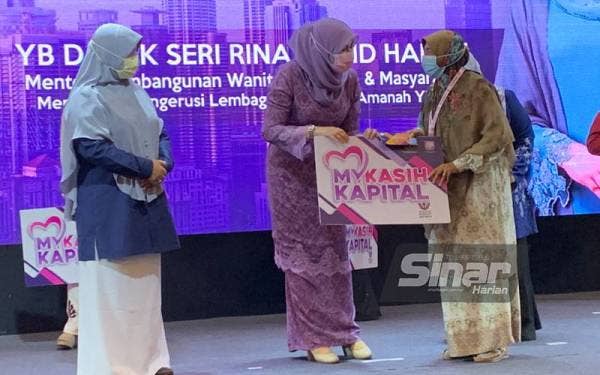 Rina (tengah) melakukan gimik penyampaian geran Program Mykasih Kapital sebanyak RM500 seorang kepada peserta yang hadir pada Program MyKasih Kapital anjuran Yayasan Kebajikan Negara (YKN) di Hotel Perdana, Kota Bharu pada Rabu.