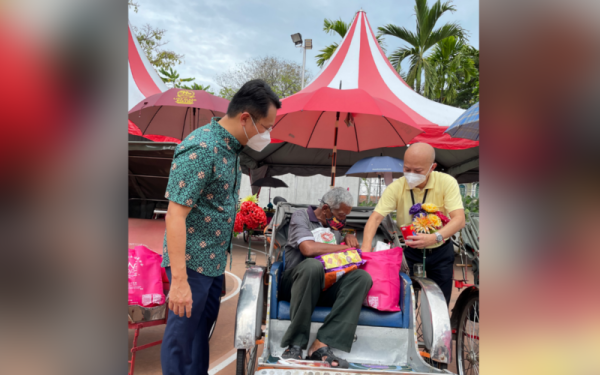 Sui Hau (kanan) menyerahkan bantuan bakul makanan kepada salah seorang pengayuh beca sambil disaksikan oleh Soon Hin (kiri).
