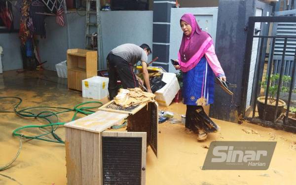 Busyral Huda membantu suami membersihkan sisa lumpur di hadapan rumahnya di Taman Pelindung Perdana yang dilanda banjir kilat pada awal pagi Jumaat.