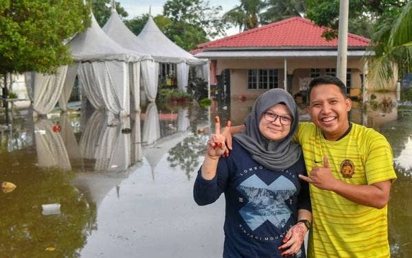 Muhammad Adib Fikri dan isterinya, Nur Fatin Liyana tetap ceria walaupun majlis kenduri perkahwinan mereka terjejas dengan banjir di Kampung Bukit Changgang yang berlangsung semalam. - Foto Bernama