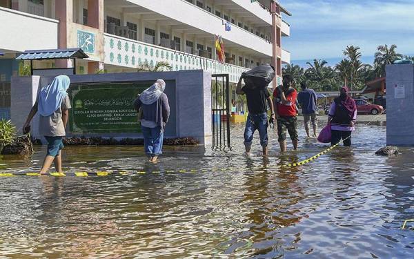 Mangsa banjir meredah takungan air banjir di pintu masuk pusat penempatan sementara (PPS) Sekolah Rendah Agama Bukit Changgang pada Selasa. - Foto Bernama