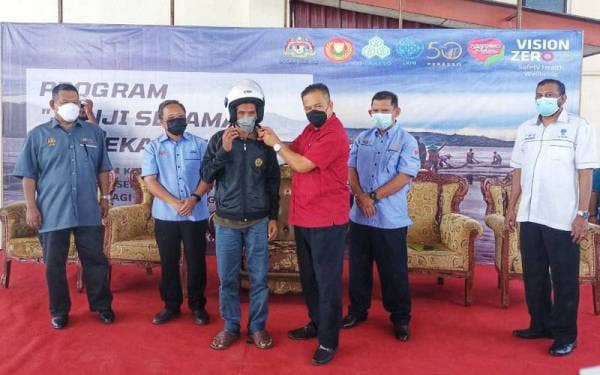 Azman memakaikan topi kaledar kepada penerima yang hadir di Program Janji Selamat Kekal Selamat di Sektor Perikanan bersama nelayan Kuala Kedah di Kompleks LKIM, Kubang Rotan di sini pada Isnin.