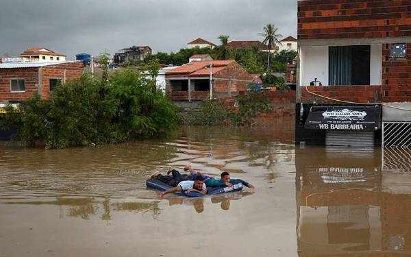 Dua penduduk terpaksa menggunakan tilam terapung untuk meredah banjir di Itapetinga. - Foto AFP