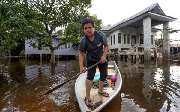 Penduduk setempat Adam Faiz Izham Musa ,14, kembali ke rumahnya setelah keadaan banjir semakin pulih ketika tinjauan di Kampung Terusan. - Foto Bernama