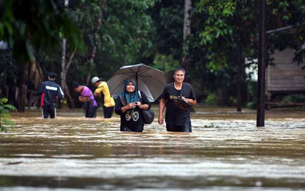 Mangsa banjir meredah air banjir untuk ke pusat pemindahan banjir (PPS) selepas rumah mereka dinaiki air di Kampung Pasir Raja di sini hari ini.