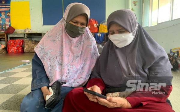Zizah (kanan) dan Alimah melihat perkembangan banjir di seluruh negeri menggunakan telefon bimbitnya semasa berada di PPS SMK Ayer Lanas pada Jumaat.