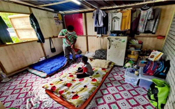 Mohamad Zahim menyapu pondok kecilnya sambil diperhatikan anaknya.