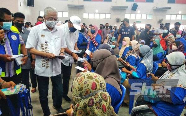 Ismail Sabri (kiri) mengagihkan bayaran wang ihsan kepada mangsa banjir di Parlimen Temerloh di Dewan MPT dekat Lanchang pada Sabtu.
