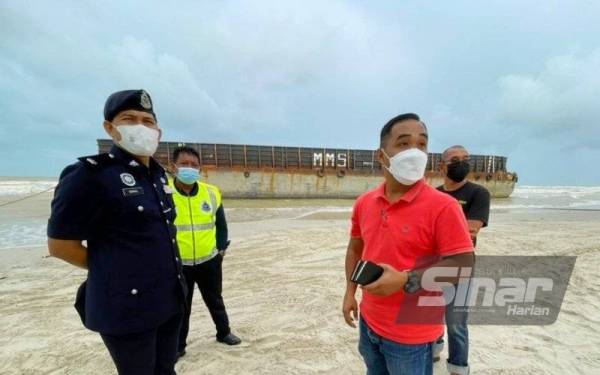 M Fakrul Razzi (kanan) bersama Mohamad Ismail (kiri) meninjau tongkang MMS 009 bernilai RM6 juta yang tersadai di Pantai Melawi, Bachok pada Isnin.