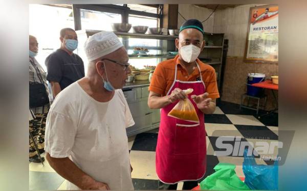 Hassan (kiri) melihat salah seorang pekerjanya membungkus makanan kepada pelangan di kedainya di sini.