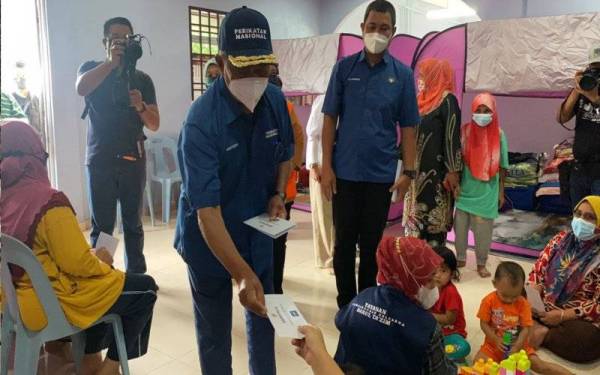 Muhyiddin menyerahkan sumbangan kepada mangsa banjir semasa meninjau pusat pemindahan sementara (PPS) Balairaya Kampung Jawa di Lenga, Muar pada Rabu.