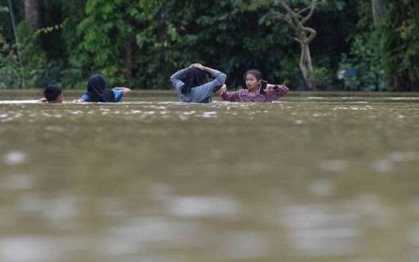 Penduduk meredah air akibat banjir besar. - Foto Bernama